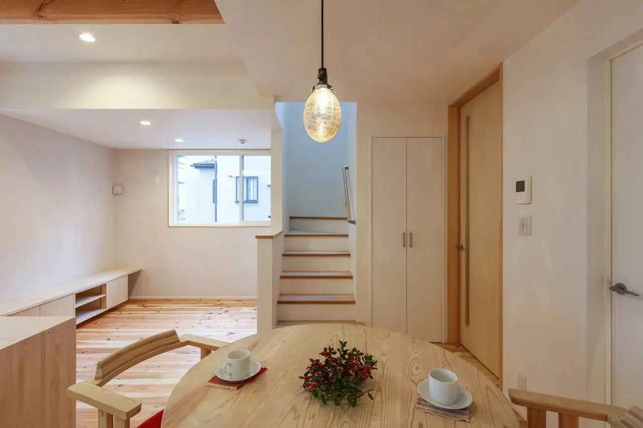 無垢杉材のフローリングと漆喰の白壁が明るいLDK。手前には円形の木製ダイニングテーブルとガラスのペンダントライト、奥には階段と造作テレビボードを配置したナチュラルな戸建てリノベーション。株式会社アイ・シー・ジーの施工事例。