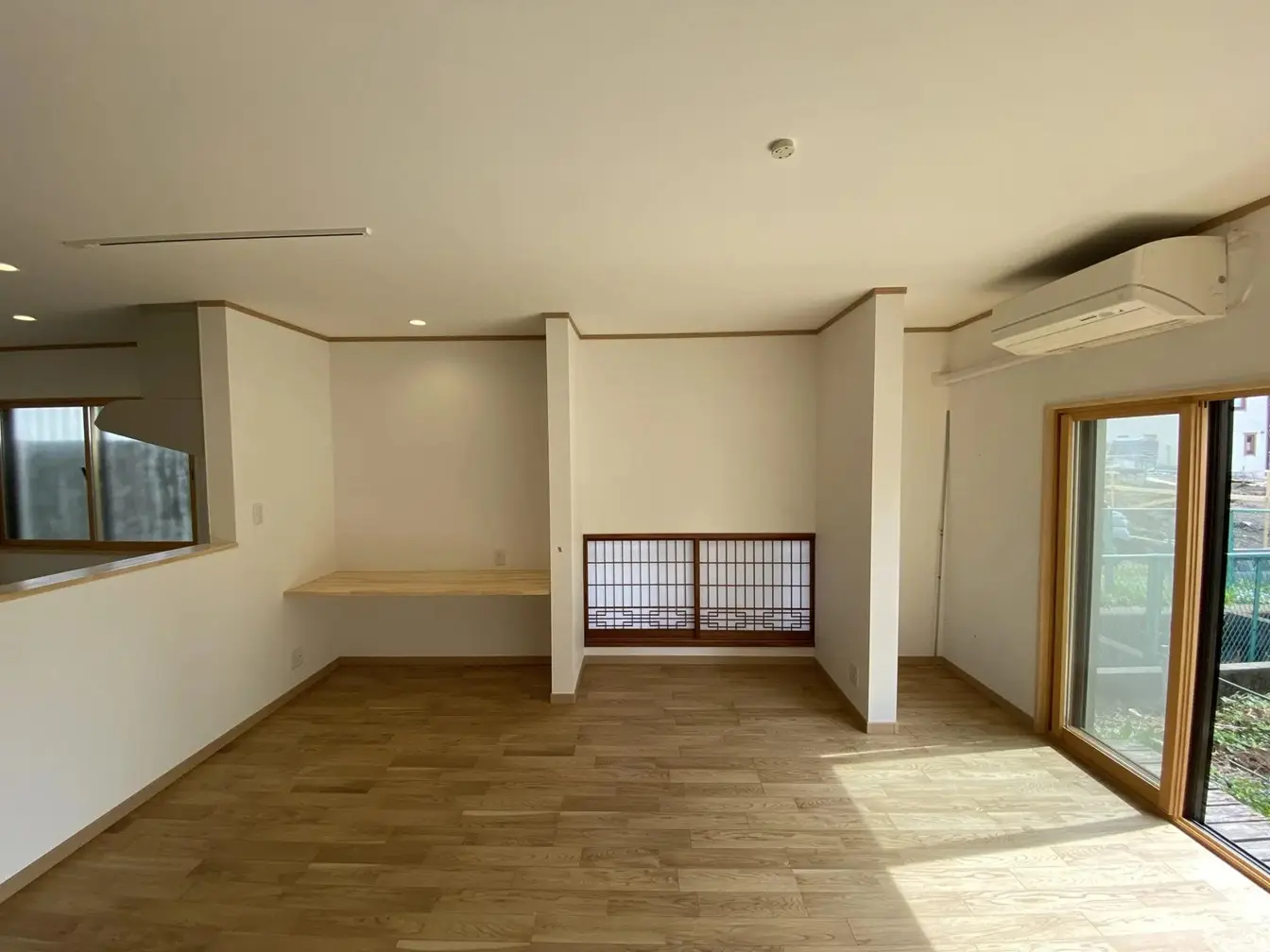 白い対面キッチンと無垢材のフローリングで構成されたLDK。背面の和室には既存の欄間と障子を再利用して配置し、現代的な設備と伝統的な意匠を融合させている。家事動線と家族の交流に配慮した、築40年の戸建てリノベーションの内観