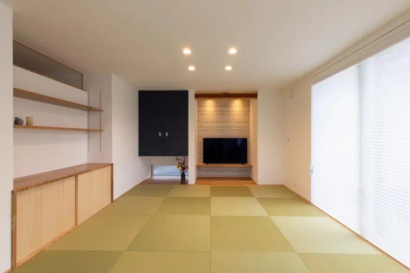 小林創建のリノベーション事例。縁なし畳を敷き詰めた広々とした和モダンのLDK。テレビ背面にはボーダータイルのアクセントウォールと間接照明を施し、洗練されたくつろぎの空間を演出している。