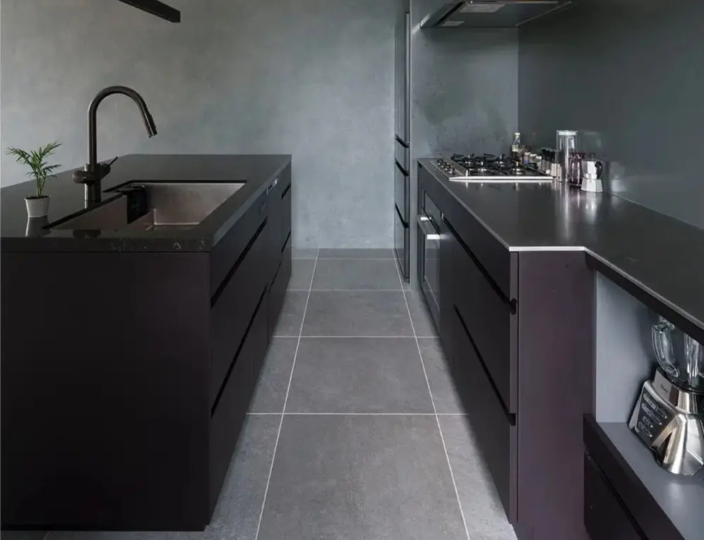 黒いキャビネットのⅡ型キッチン。手前はクオーツ天板と黒いシンク、奥はステンレス天板とコンロ・オーブン。床はグレーのタイル。ダークトーンでまとめたモダンなホテルライク空間。インテリックス空間設計のリノベーション事例。