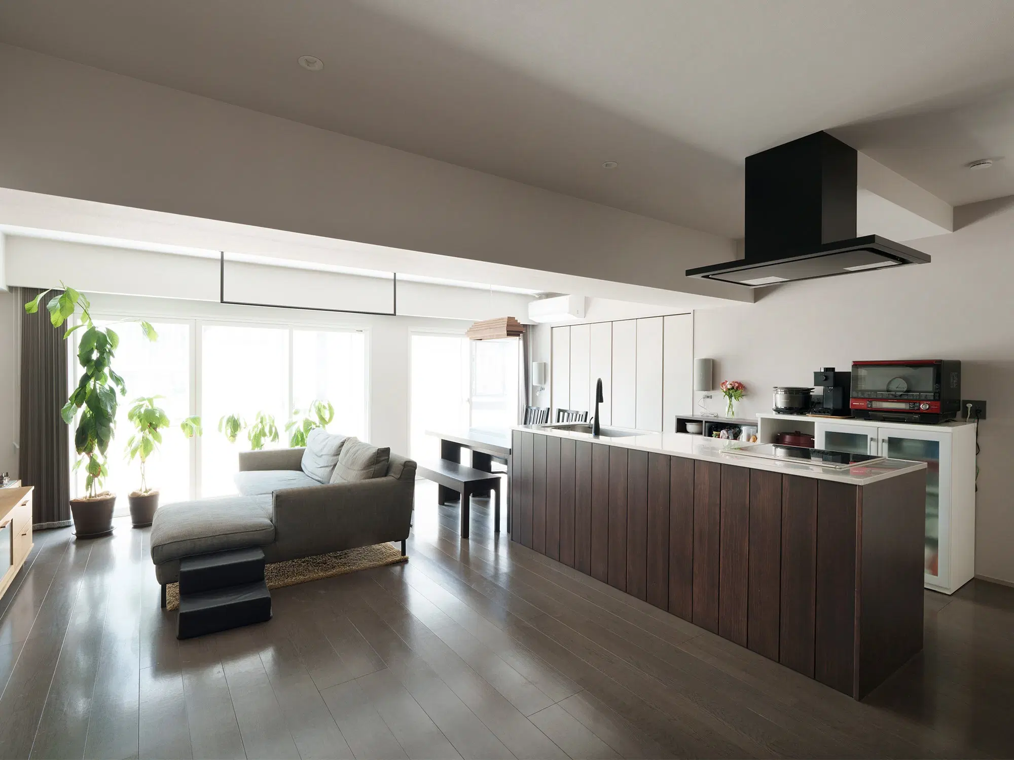 リノベーションで広くなったLDKと、回遊できるアイランドキッチンの写真。ダークブラウンの木目が落ち着いた雰囲気の、モダンで開放的な空間です。