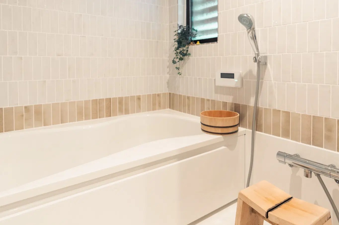 ハーフユニットバスを採用し、壁面を白いタイルとベージュのボーダータイルで仕上げた浴室。木製の桶と椅子が温かみを添え、ヴィンテージホテルのようなラグジュアリーな空間を演出したマンションリノベーション。可美建築の施工事例。