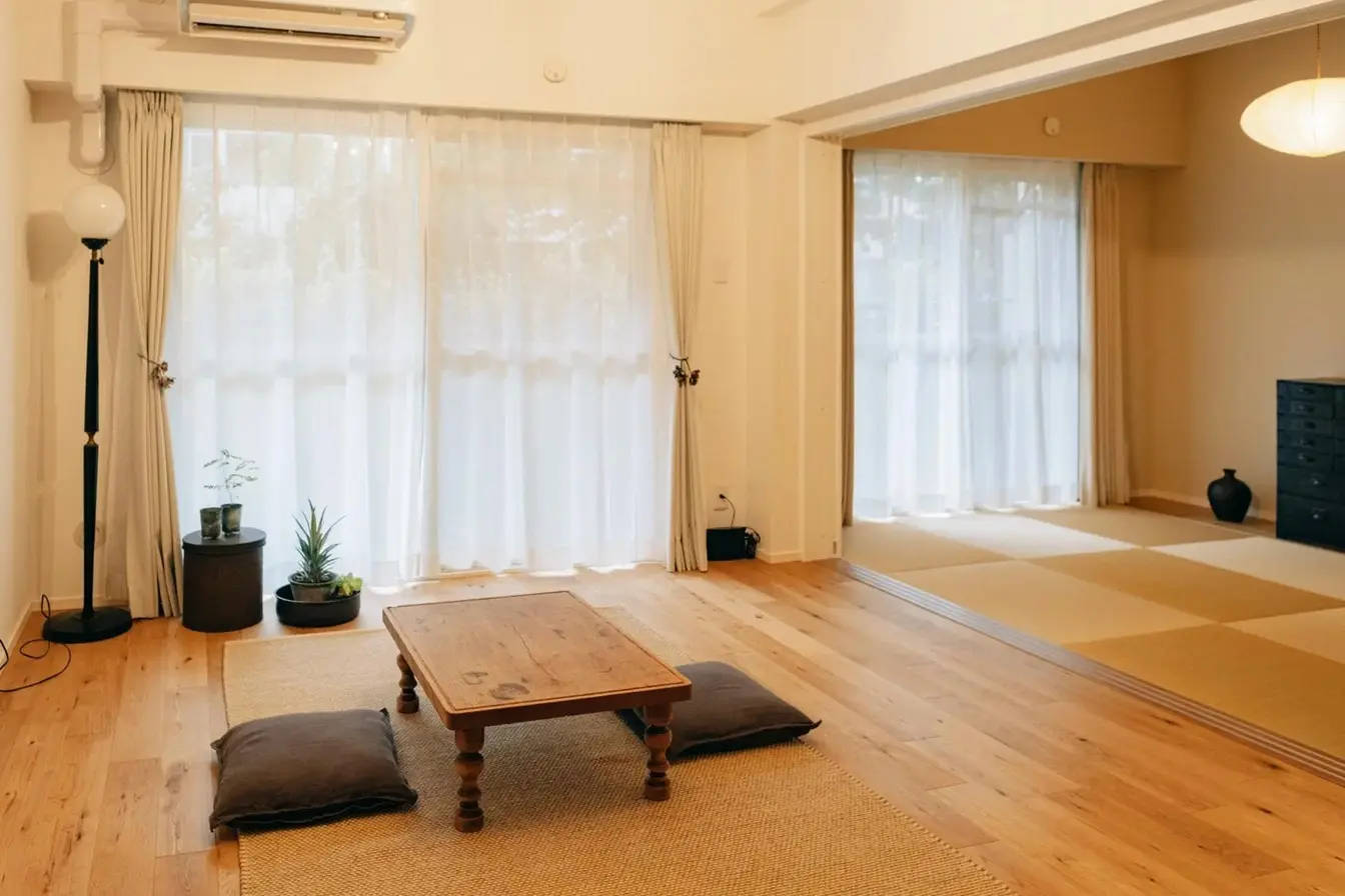 fujitacaリノベーションによる施工後の内観。フローリングのリビングと奥の和室が段差なくフラットに繋がり、開放感がある。和室には黒い箪笥と球状の照明が置かれ、アンティークな雰囲気が漂う。