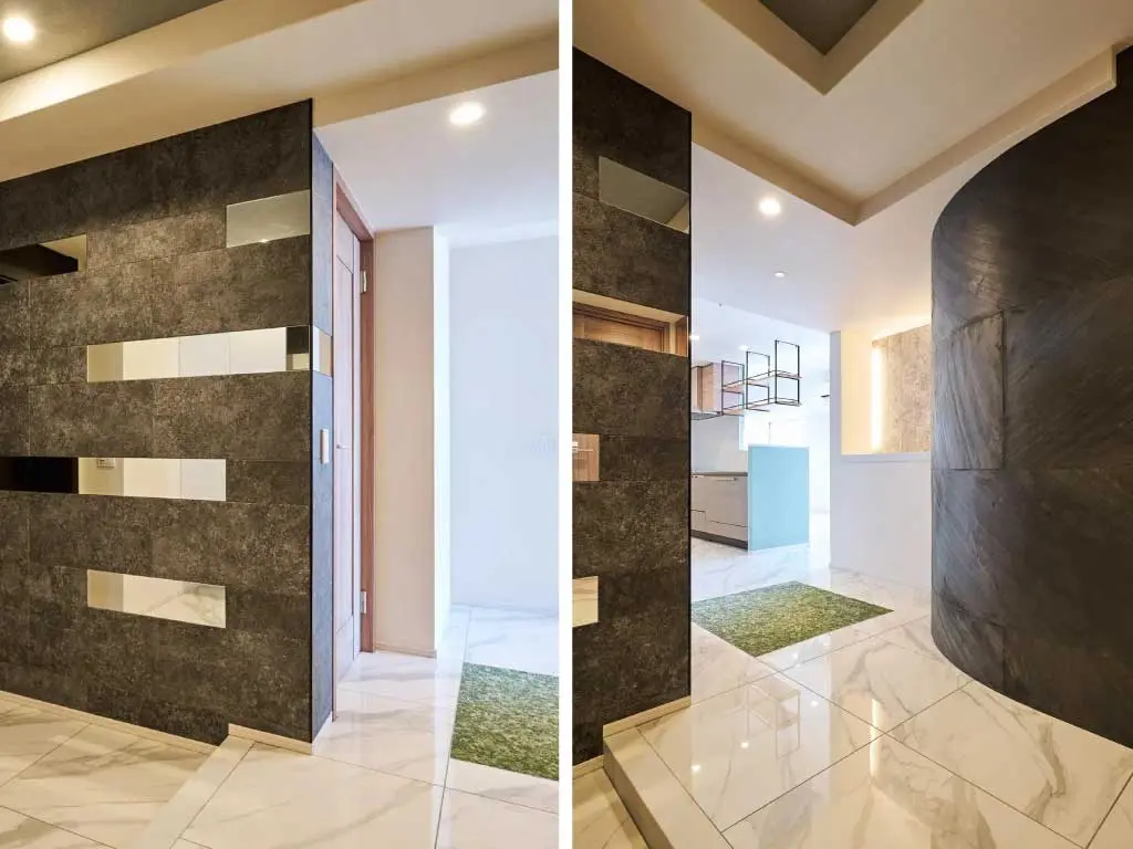 マンションリノベーションの玄関写真。左壁はダークグレーのタイルと鏡を組み合わせたデザイン貼りで、奥には白い曲面壁（R壁）が見える。床は大理石調。