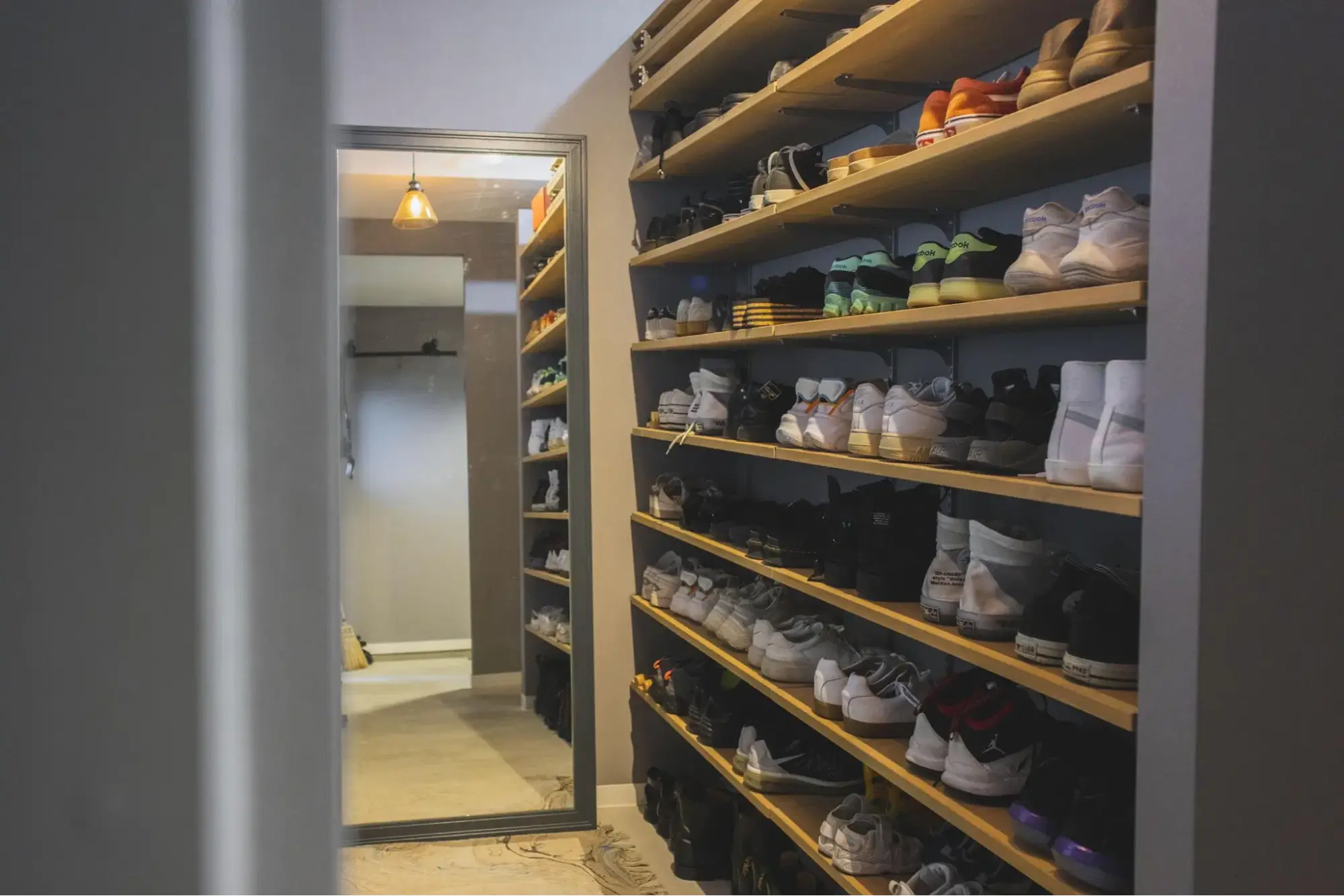 玄関から続く土間仕上げの広々としたシューズクローゼット。壁一面の木製棚には、アパレル関係のご夫婦が所有する多くの靴がショップのようにディスプレイされている。奥には姿見を置き、身支度もスムーズなヴィンテージ空間。パパママハウスの施工事例。