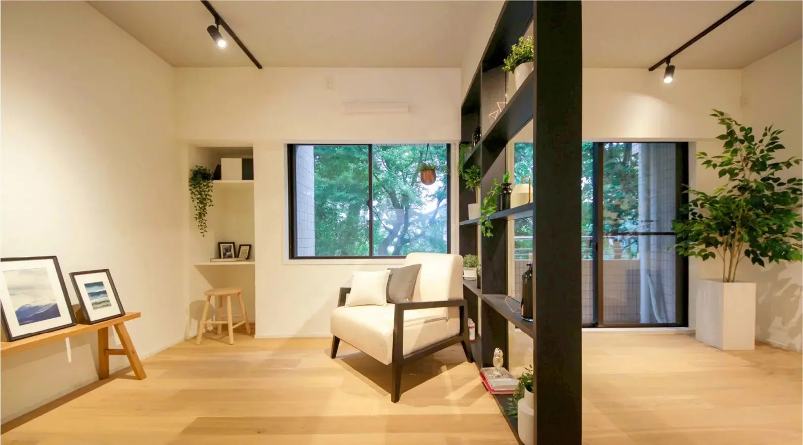 黒い枠のディスプレイ棚を間仕切りとして設置したリビング。大きな窓から借景の緑を取り込み、手前には白いアームチェアと木製のフローリングが広がる。田中建設の施工事例。