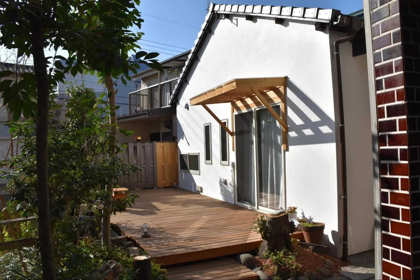 有限会社スケールメイクスのリノベーション事例。築60年の古民家の外壁を無添加漆喰で白く塗り直し、庭には大きなウッドデッキと木の庇を新設。既存の瓦屋根の趣を残しつつ、明るく再生された外観。
