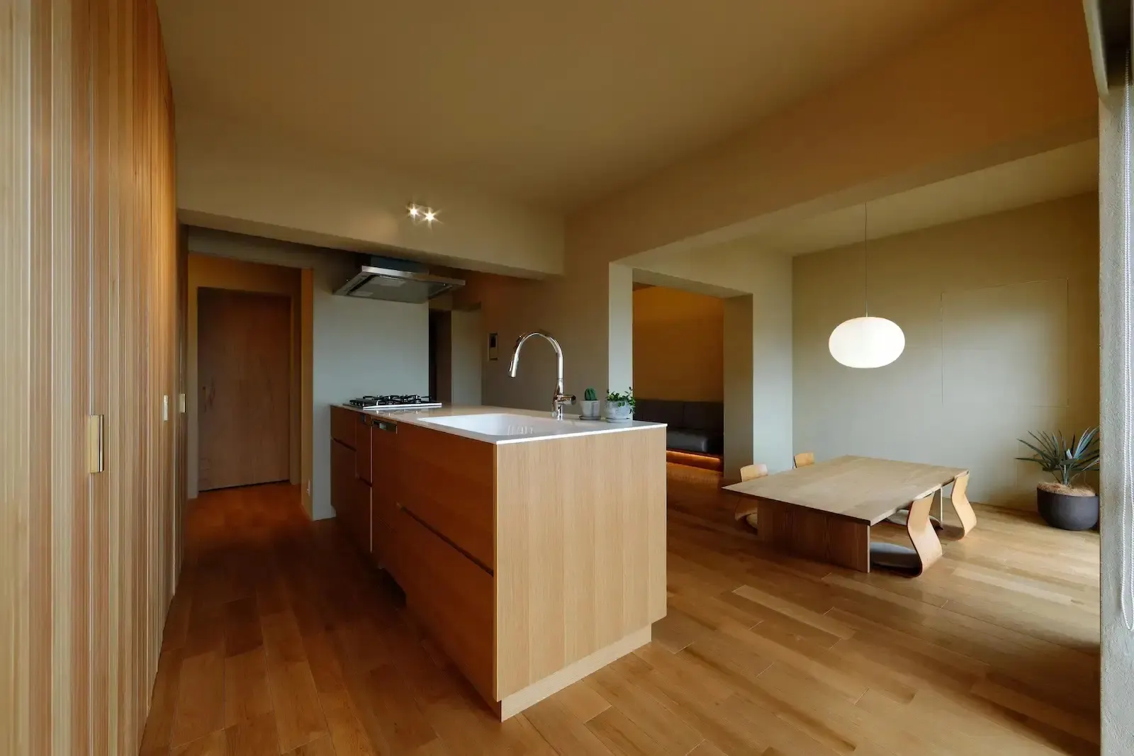 ひかり工務店の事例。天井の低さを活かし、洞窟のような籠り感を演出したLDK。ジョリパット壁と木製アイランドキッチンが調和。座卓と丸い照明を配した和モダンの空間で、スイッチを隠し生活感を排したミニマルなマンションリノベーション内観。