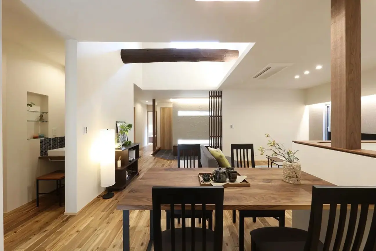 吹き抜けの高い天井に架かる、古民家ならではの太い丸太梁が印象的なダイニング。トップライトから自然光が降り注ぎ、無垢材のフローリングと木製家具を照らす、明るく開放的な和モダンの空間。