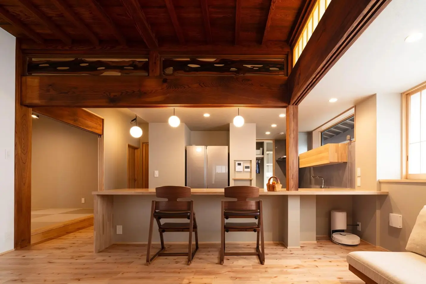 古民家の特徴である立派な梁と欄間を残しつつ、モダンなカウンターキッチンを設置したLDK。丸いペンダントライトと無垢材のフローリングが調和し、新旧の素材が融合した温かみのある内観。