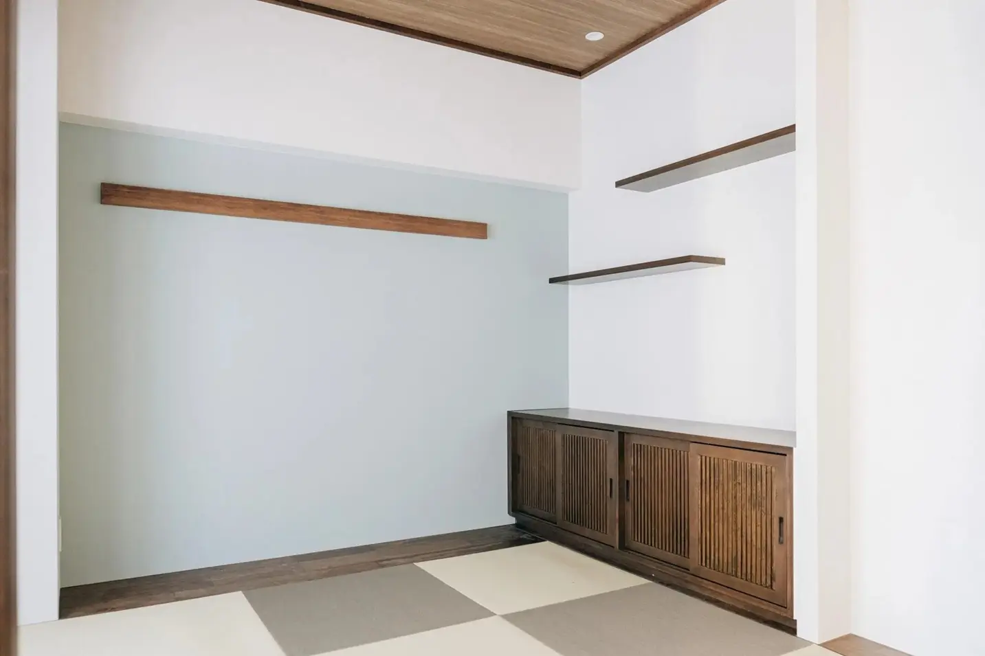 市松模様の畳と、格子戸の木製ローボードが古民家のような風情を醸し出す和室。壁面には飾り棚を設置し、淡いブルーのアクセントクロスでモダンな印象をプラス。マンションで懐かしい暮らしを実現した、fujitacaリノベーションの施工事例。