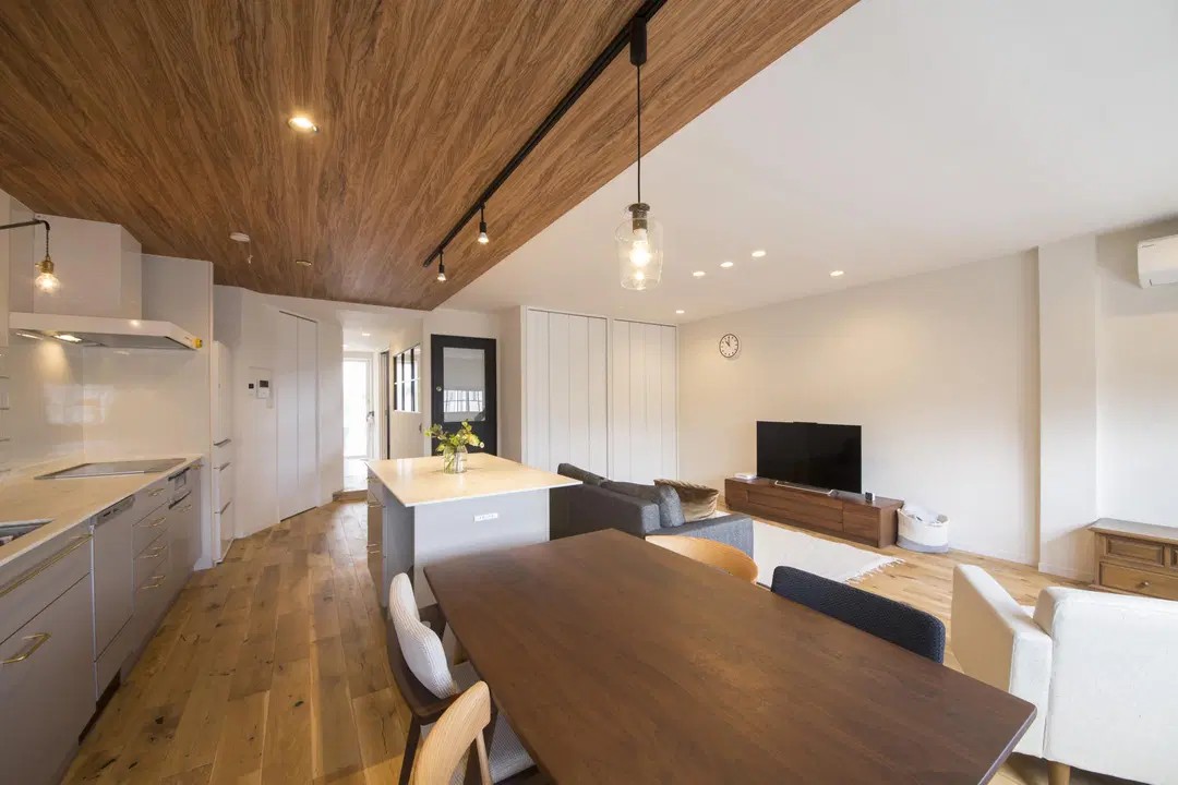 パパママハウスのリノベーション事例。キッチンの天井に木目をあしらい空間をゾーニングしたLDK。グレーの対面キッチンやペンダントライトが、シンプルナチュラルな空間に馴染んでいる。