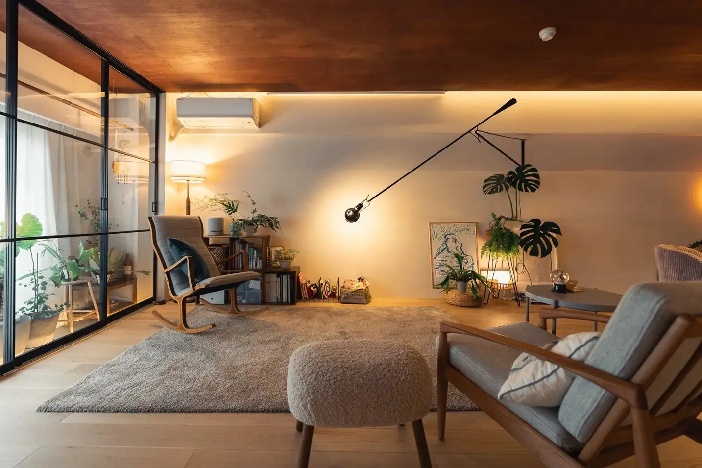 マホガニー色に塗装したラワン材の天井と間接照明が、ヴィンテージホテルのような重厚感を醸し出すリビング。黒枠のガラスパーティションや、特徴的なロングアームの照明、木製家具が調和したリノベーション空間。可美建築の施工事例。