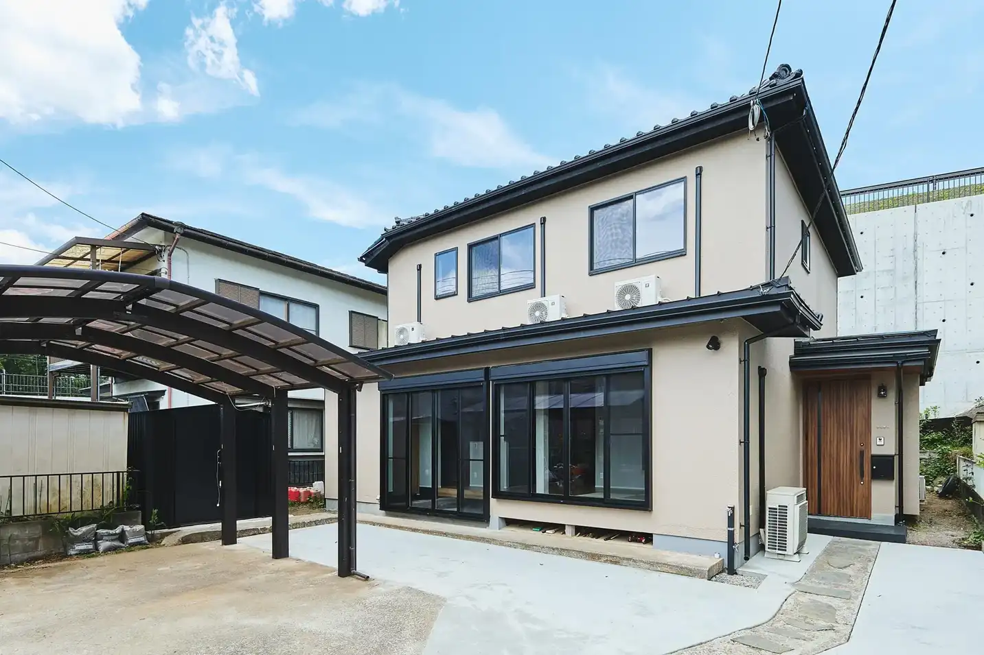 フルリノベーション後の戸建て外観。ベージュの吹付外壁と木目調の玄関ポーチ、カーポートを備えた2,800万円台の改修事例