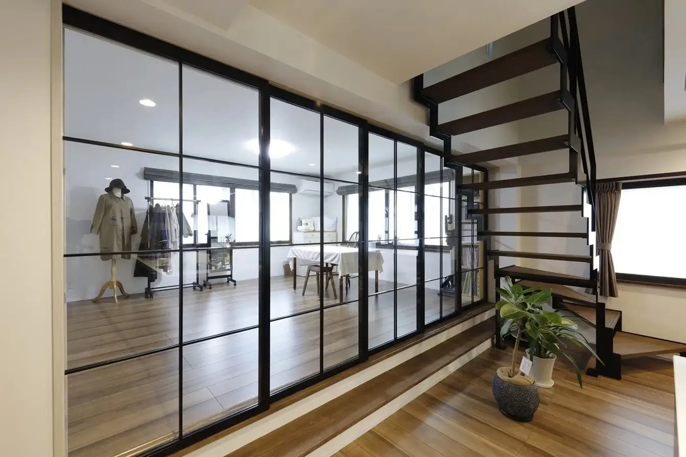 あなぶき・きなりの家株式会社のリノベーション事例。リビング横に設けた、黒い格子のガラス戸で仕切られたワークスペース。手前には空間のアクセントとなる木と黒い鉄骨のスケルトン階段がある。