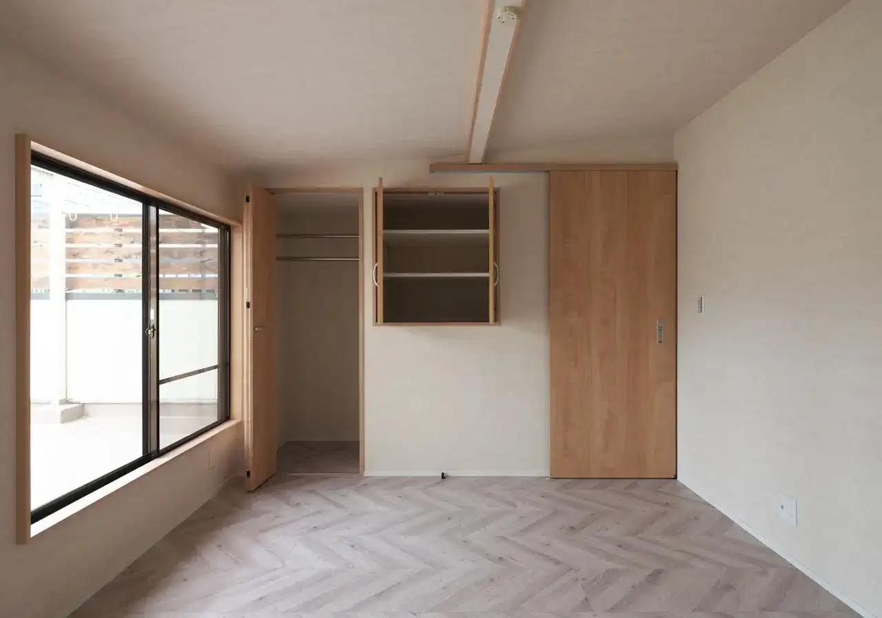 アイ・シー・ジーによるリノベーション後の寝室。淡い色味のヘリンボーン床と木製の収納扉が温かみを演出している。大きな窓から自然光が差し込み、バルコニーへと視線が抜ける明るい空間。