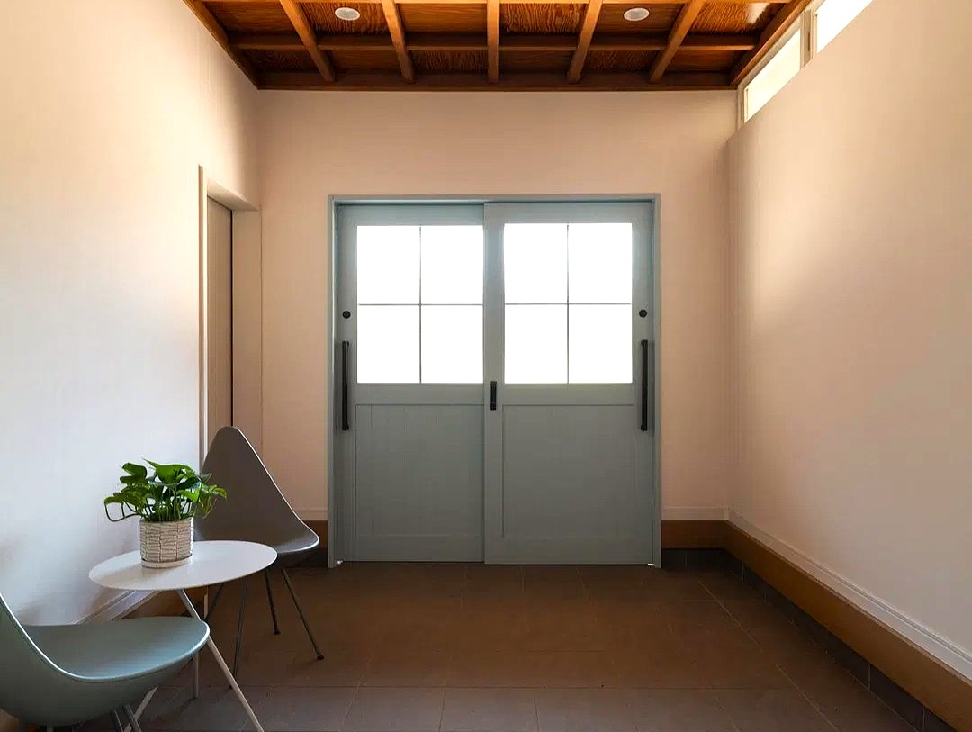 茨城の築50年戸建てフルリノベーション後。既存の格天井を活かした和モダンな玄関土間。正面には水色の格子付きガラス引き戸、左手にはモダンなチェアとテーブル、観葉植物を配置。懐かしさと現代デザインが融合した空間。株式会社AS IT ISのリノベーション事例