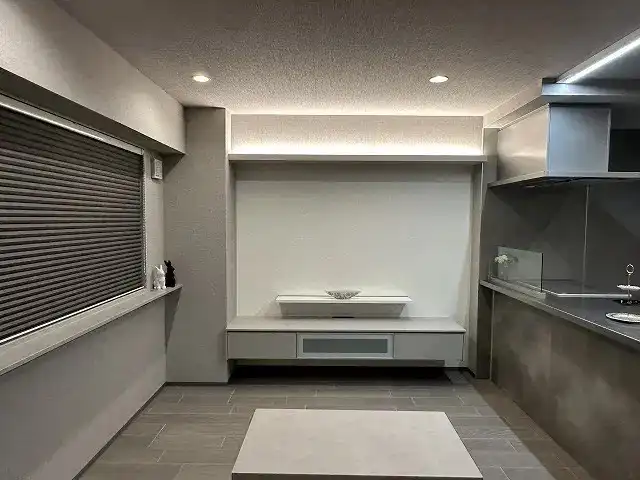 グレーで統一されたリビングの写真。床はグレーのタイル張りで、壁には造作のテレビ台が設置されている。天井には間接照明が組み込まれている。