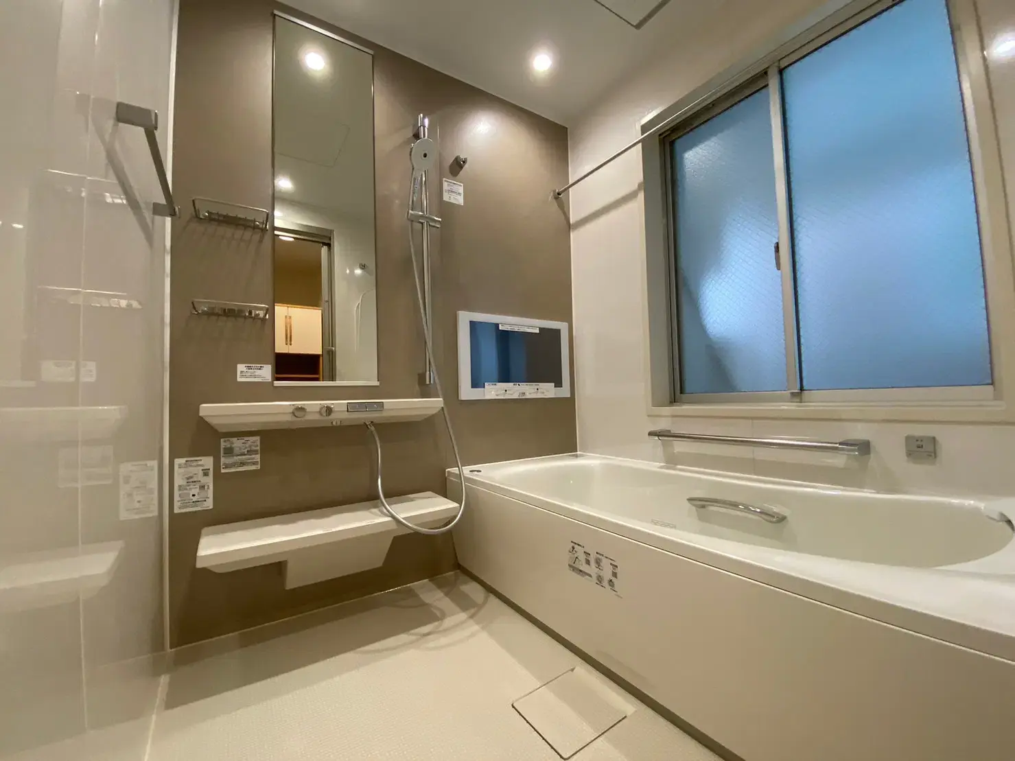 落ち着いたブラウンの壁パネルと浴室テレビが特徴的な、TOTOの高級システムバス「シンラ」。大きな窓と鏡で開放感を持たせ、ラグジュアリーなバスタイムを演出する鉄骨造戸建てのリノベーション。有限会社スケールメイクスの施工事例。
