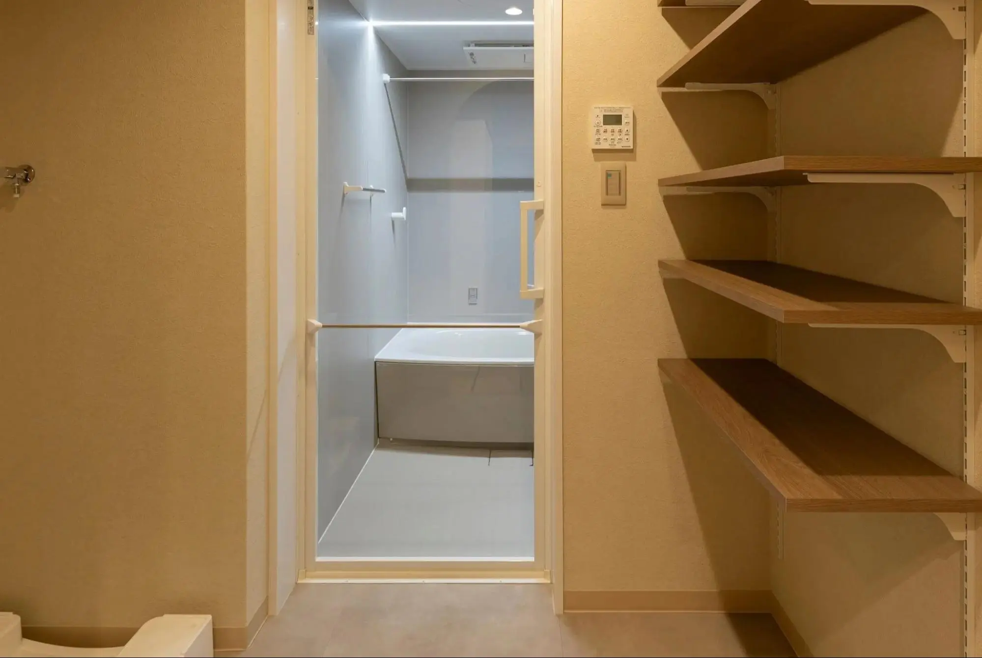 透明なガラス扉がホテルライクな雰囲気を演出する浴室と、壁面に大容量の可動棚を設置した使い勝手の良い脱衣所。ベージュのクロスで上品に仕上げたマンションリノベーション。an cubeの施工事例。