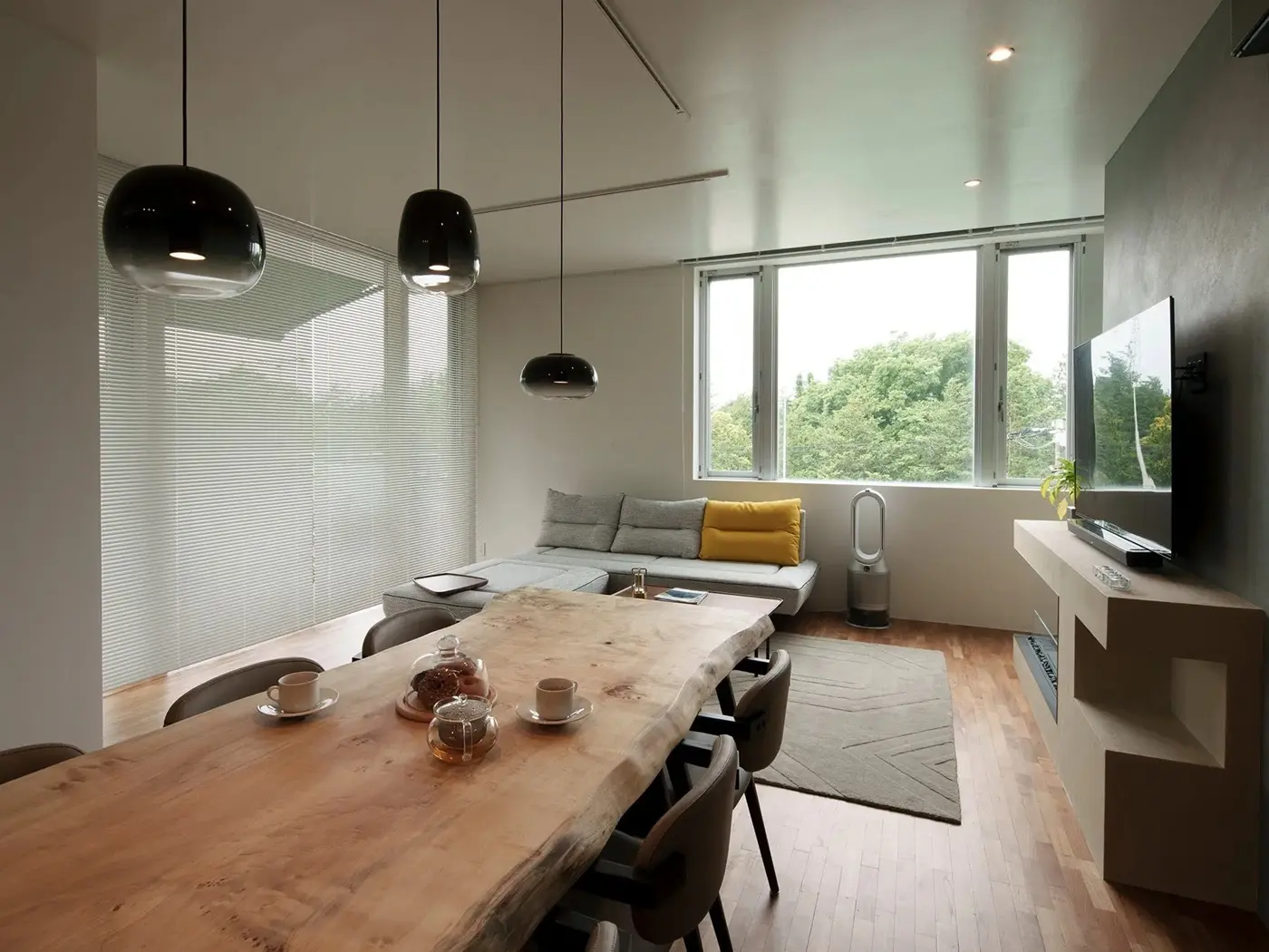 窓一面に広がる木々の緑と調和する、一枚板のダイニングテーブルが主役のLDK。黒いペンダントライトやシンプルモダンな家具を配置し、外の景色までインテリアの一部としたメゾネットリノベーション。インテリックス空間設計の施工事例。