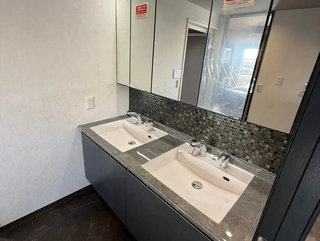 グレーの石目調カウンターに2つのボウルを並べた、高級感あふれるホテルライクな洗面台。鏡とカウンターの間に施したシックなモザイクタイルが、洗練されたスタイリッシュな空間を演出している。設備やデザインにこだわり抜いて完成した、an cubeのマンションリノベーション事例。