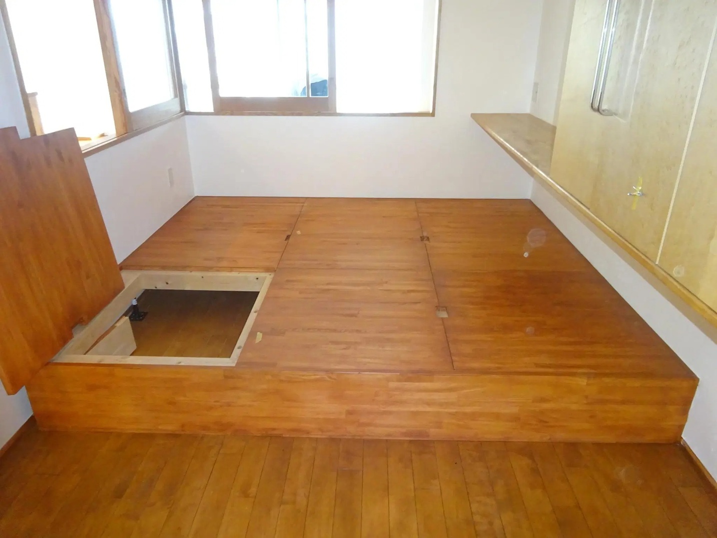 スケールメイクスによるリノベーション後の寝室。壁全面が無添加漆喰で仕上げられ、床下収納を備えた木製の小上がりが造作されている。蓋を開けて内部の収納スペースが見えている状態。