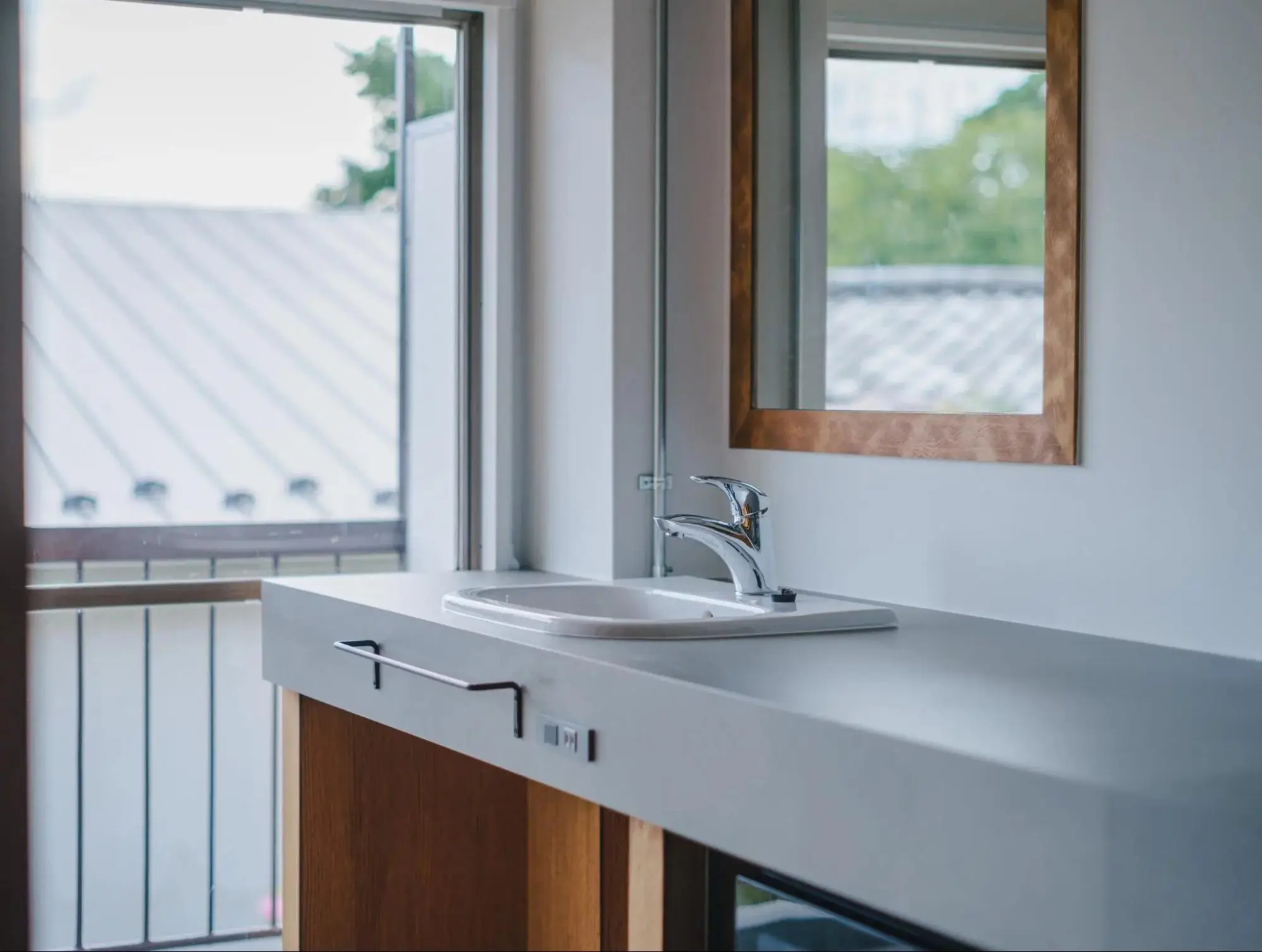 窓から差し込む自然光が気持ち良い、海外のモーテルのような雰囲気の洗面空間。グレーの天板に木枠の鏡を合わせたHOTEL仕様のデザインで、キッチンからカウンターがフラットに繋がっている。アズ建設によるワンルーム賃貸マンションの施工事例