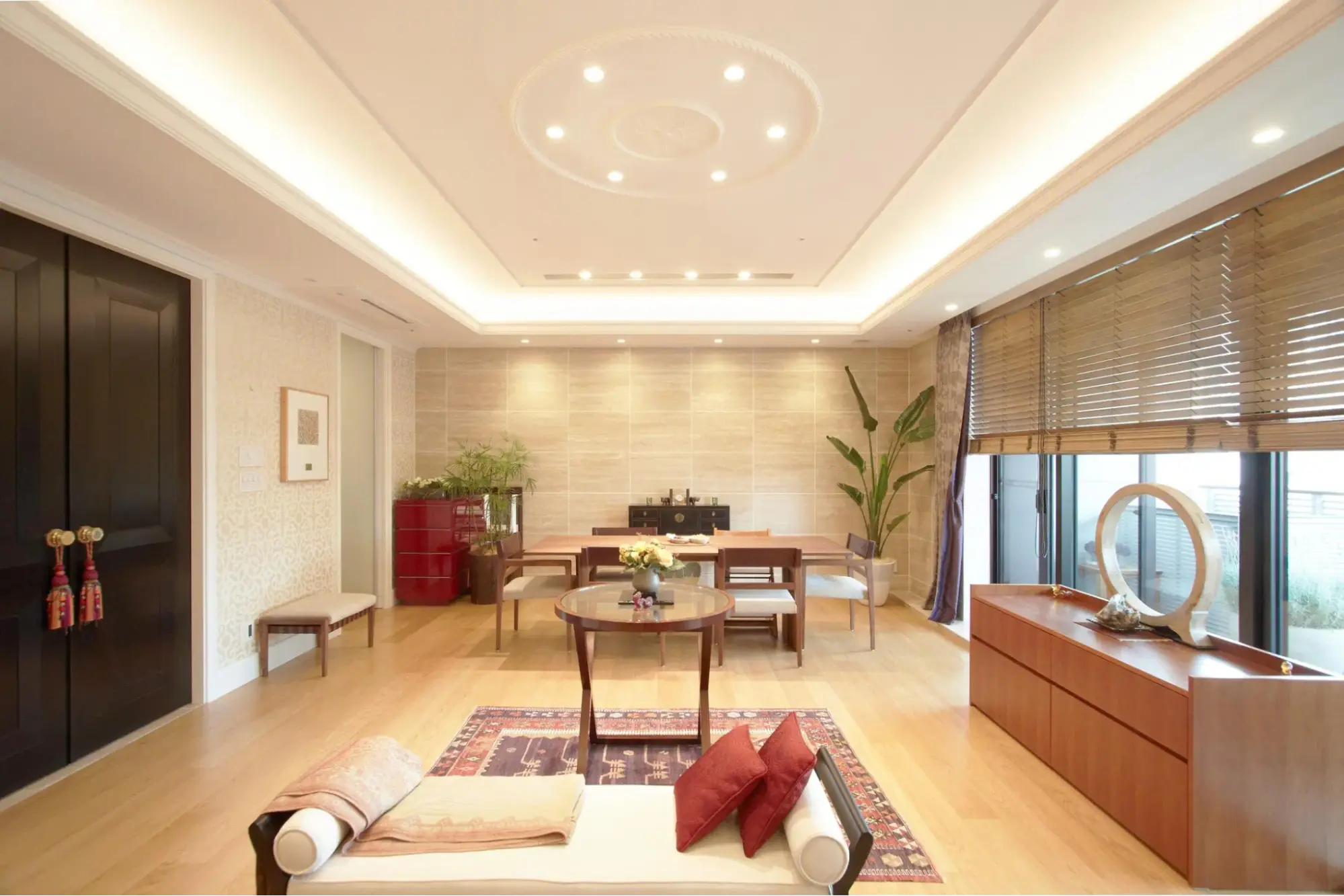 美しい折り上げ天井の間接照明が優雅な雰囲気を演出する、広々としたリビングダイニング。アジアンテイストのラグや家具、木製ブラインドを組み合わせ、まるで高級リゾートホテルのような洗練された空間に仕上げている。株式会社リノベーション東京の施工事例。