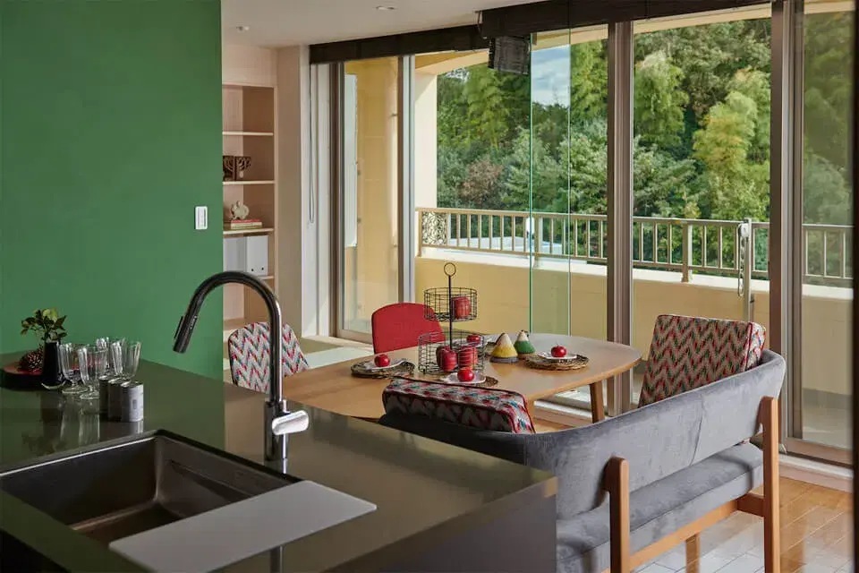 大きな窓から豊かな緑の景色を楽しめる開放的なダイニングキッチン。グリーンのアクセントウォールが外の自然と調和し、子育て世代の家族がくつろげるナチュラルで明るい空間に仕上げたマンションリノベーション。株式会社ディセノの施工事例。