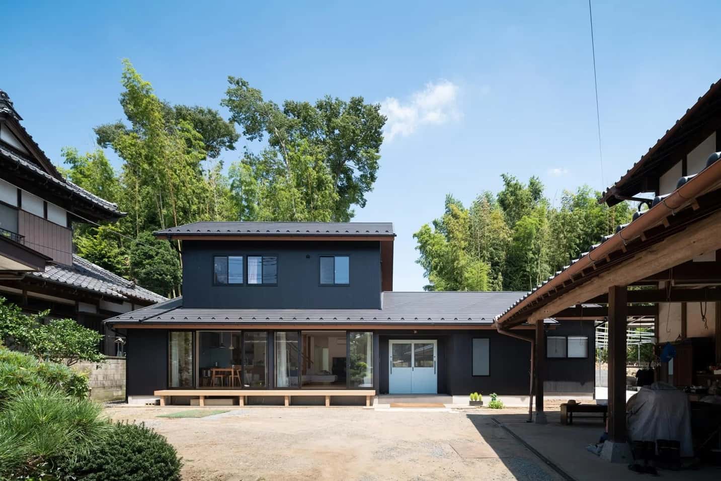 瓦屋根と黒い外壁が特徴的な2階建てのリノベーション外観。1階には大きな掃き出し窓と白い両開きの玄関ドアが設置され、隣接する古い日本家屋と調和した和モダンな佇まい。