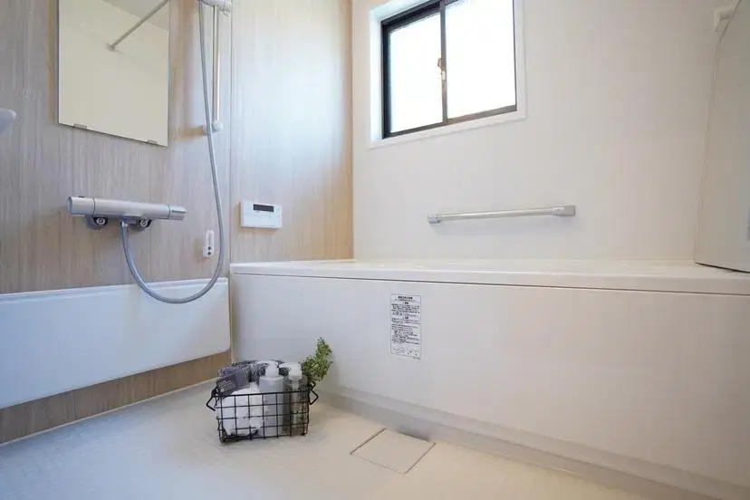 白を基調にライトベージュの木目調パネルを合わせた、シンプルで清潔感のあるユニットバス。窓から自然光が入り、横長の鏡が空間に広がりを与える。ゴミ屋敷から再生した戸建てリノベーションの1階バスルーム。My Design/株式会社Izumidaの施工事例。