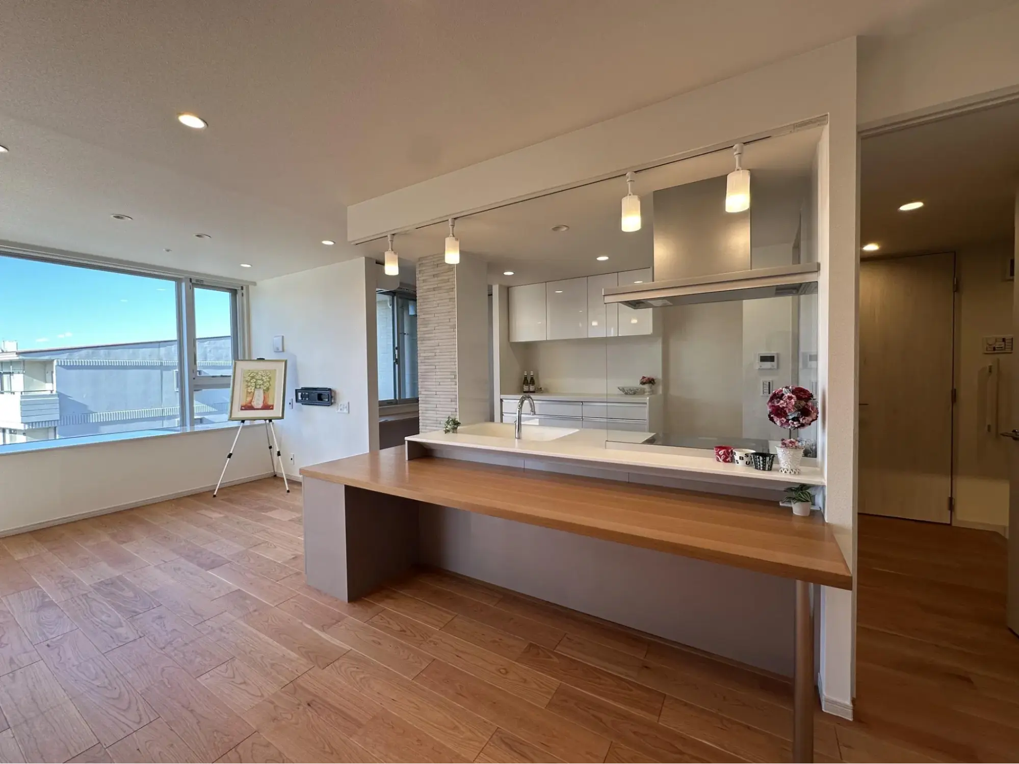 大きな窓から光が差し込む開放的なLDKの中心に配置されたオープンキッチン。前面にはご夫婦で食事が楽しめる木製のダイニングテーブルを造作し、料理中も会話が弾むナチュラルな空間に仕上げている。ライフスタイルの変化に合わせて間取りを一新した、リノベーション東京のフルリノベーション事例。