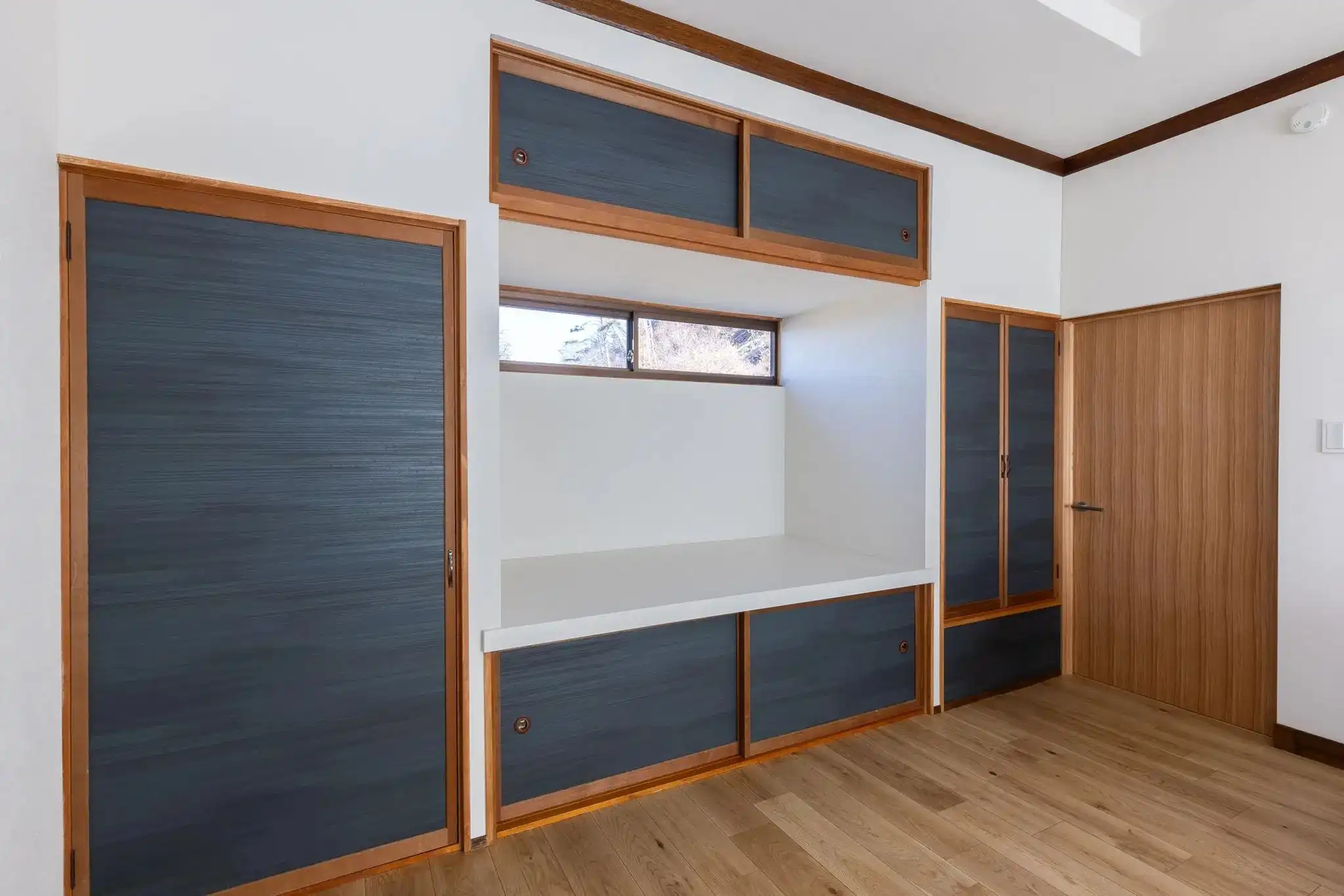 小林創建によるリノベーション後の寝室。紺色のシックな襖紙を使用した造作収納棚と引き戸が壁一面に設置され、中央に明かり取りの窓がある和モダンな空間。