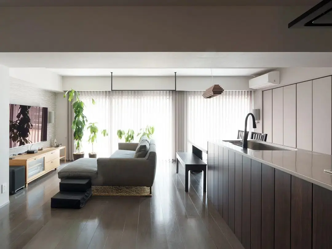 ダークブラウンの床と、縦格子の木製キッチンアイランドがあるLDK。奥の掃き出し窓には、床まである白いシアーカーテンが掛かっている。