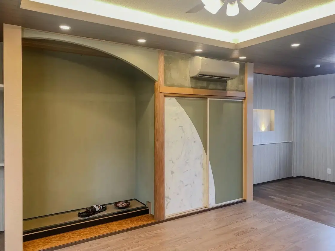 大槻建設による和モダンなリビング。職人技が光る曲線デザインの床の間と京壁仕上げが特徴。間接照明とダウンライトで演出されたリノベーション後の内観。