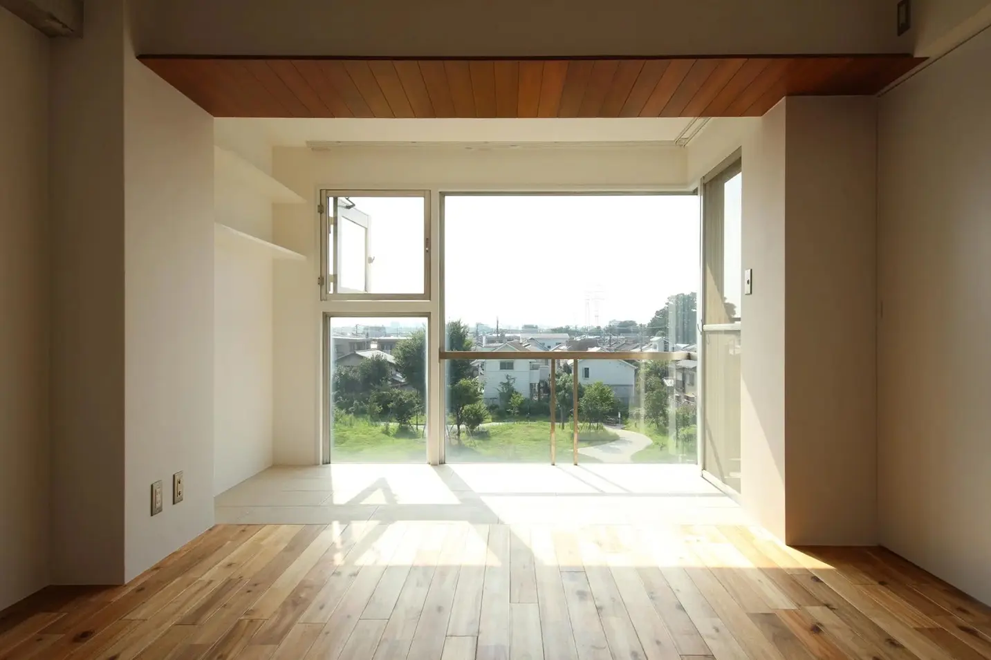 公園の緑を一望できる大きな窓から、たっぷりと自然光が差し込む明るいインナーバルコニー。窓際は白いタイル張りで、居室の無垢フローリングとフラットにつながっている。天井の木製パネルがアクセントになった開放的な空間。