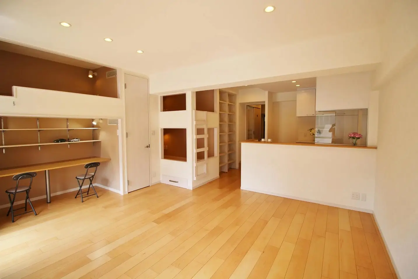 空間を最大限に活用するため、造作のロフトベッドや2段ベッドを壁面に配置したナチュラルなリビング。ロフト下にはデスクを設け、右側には家族の様子を見渡せるオープンキッチンを配置。家具を極力置かず中央のスペースを広く確保した、株式会社リノベーション東京のマンション施工事例。