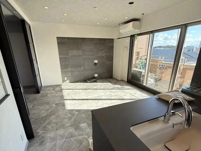 リノベーション後のリビング写真。床はグレーのタイル張りで、壁の一部には濃いグレーのタイルが貼られている。大きな掃き出し窓がある。