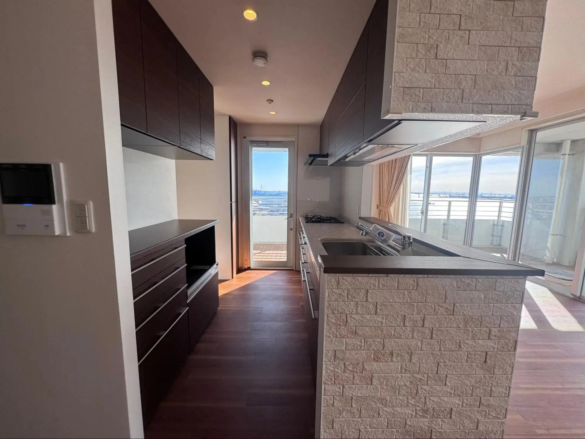 ダークブラウンのキャビネットと石目調タイルの腰壁が特徴的な対面キッチン。窓から海とみなとみらいを一望できる、ホテルライクなタワーマンションのリノベーション。LIXILのリシェルを採用。リフレネクスト横浜の施工事例。