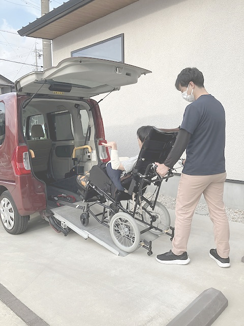 車椅子の方が車に乗るのを、ヘルパーが手伝っている写真