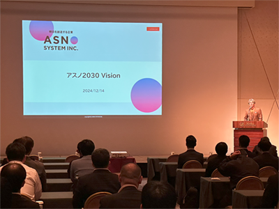 アスノ2030Vision と書かれたスライドを表示させながら、会場にいる社員に説明する齋藤武育代表取締役の写真。