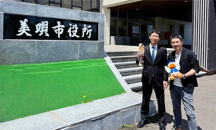 美唄市役所の前で並ぶSI事業第1本部 SIサービス部 課長 服部泰輔と地方創生企画部 部長の楠徹平の写真