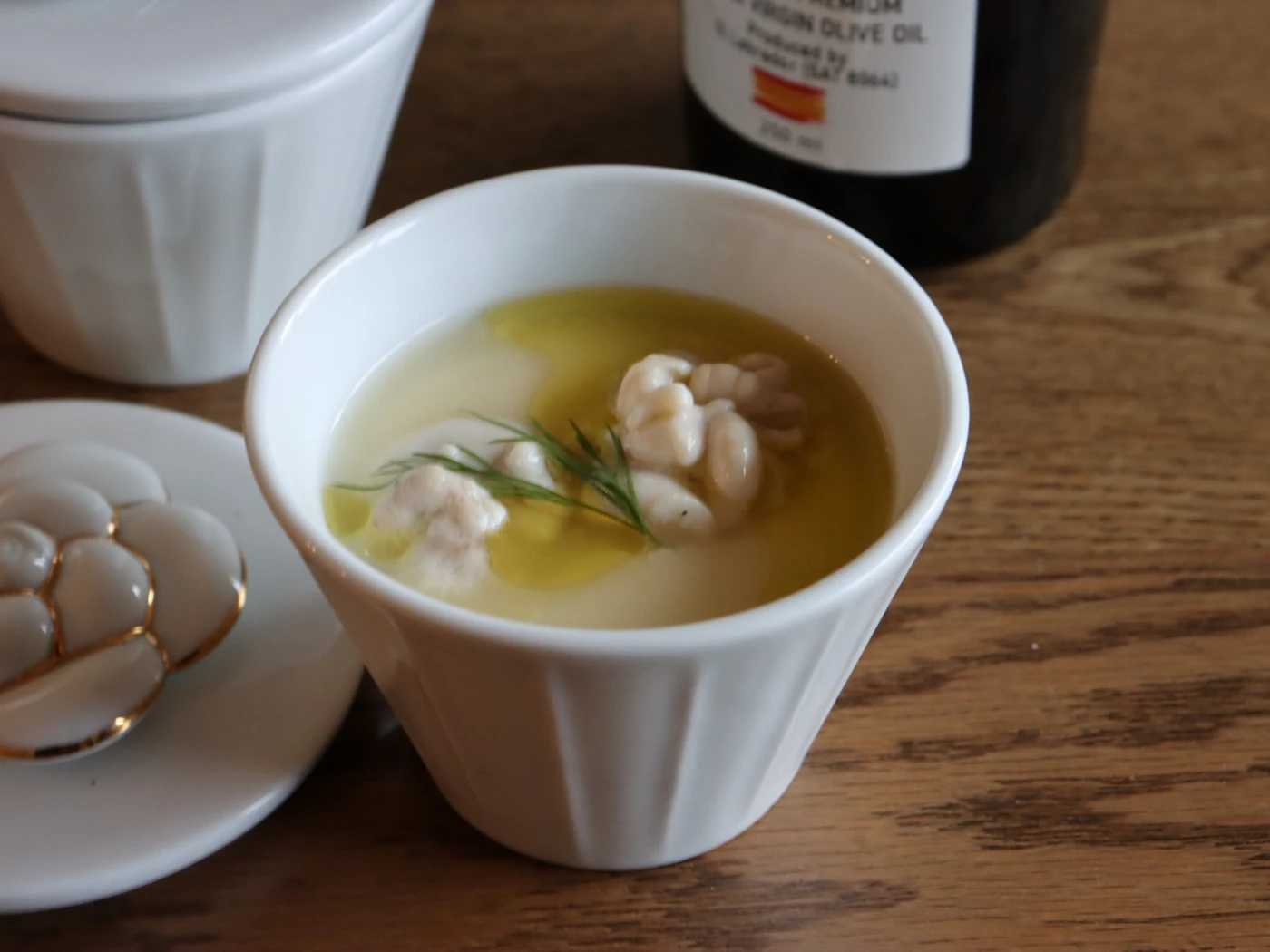Shirako flan in a white cup, topped with olive oil and dill