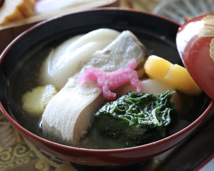 お正月の食卓。赤い漆の椀に入った博多雑煮と、重箱に詰めたおせち