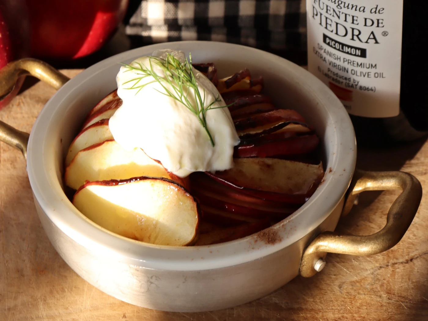 Thin apple slices baked in overlapping rows in a dish with a handle, topped with ice cream and dill