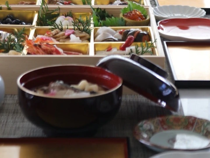 お正月の食卓。赤い漆の椀に入った博多雑煮と、重箱に詰めたおせち