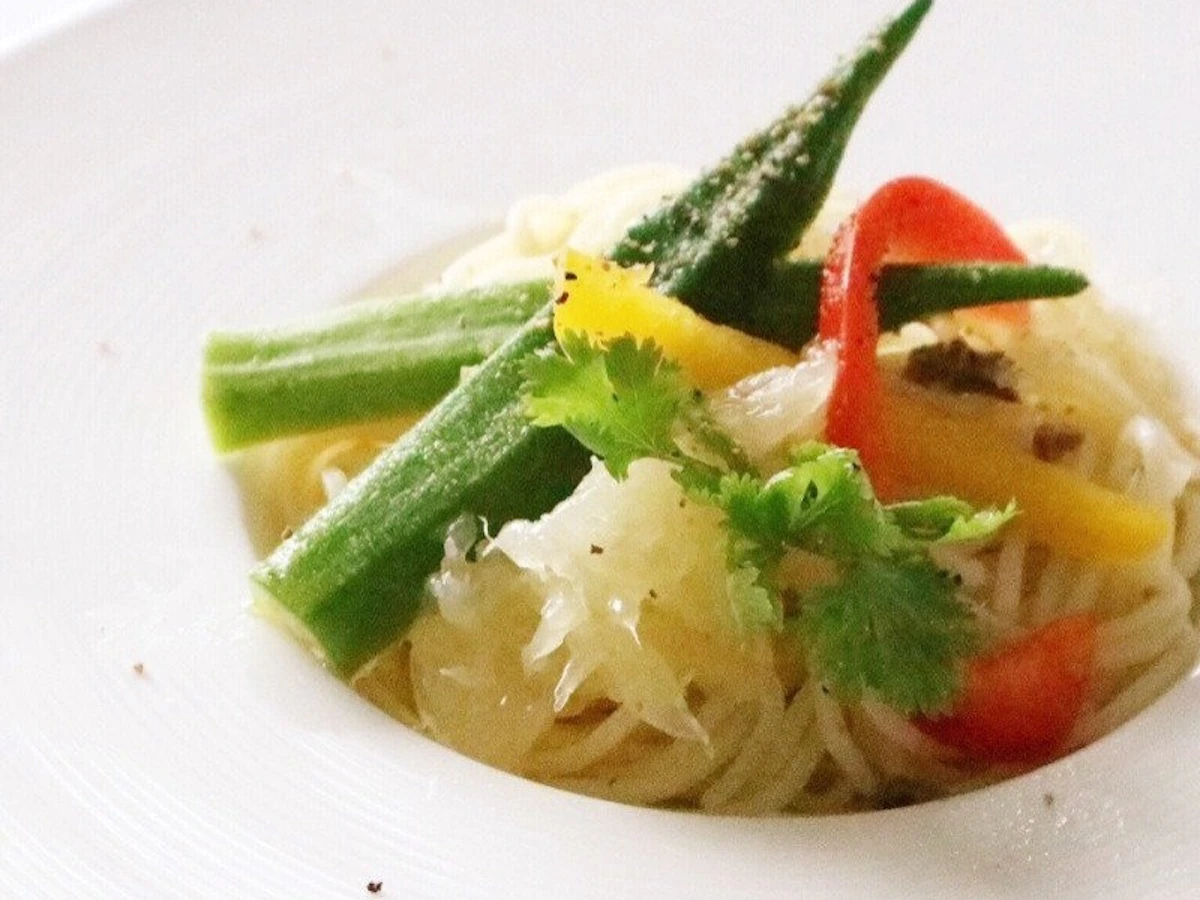 白い深皿に盛った細い麺に、ほぐしたグレープフルーツの果肉と縦半分に切ったオクラ、赤と黄色のパプリカ、パクチーをのせた冷製パスタ