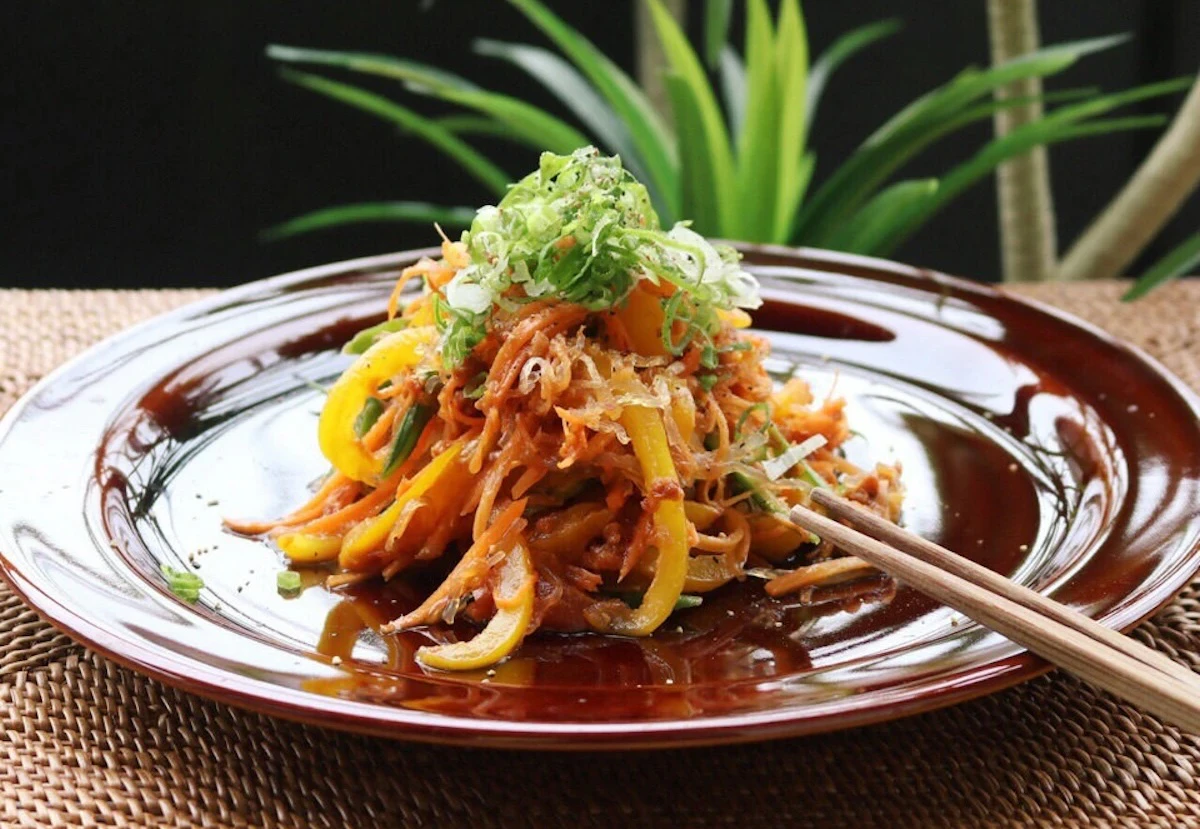 赤茶色の皿に盛り、ねぎをのせた千切り野菜と海藻麺の韓国風RAW焼きそば