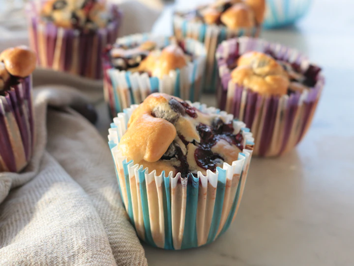 紙のカップに入った、粉砂糖をふったブルーベリーとチョコのマフィン